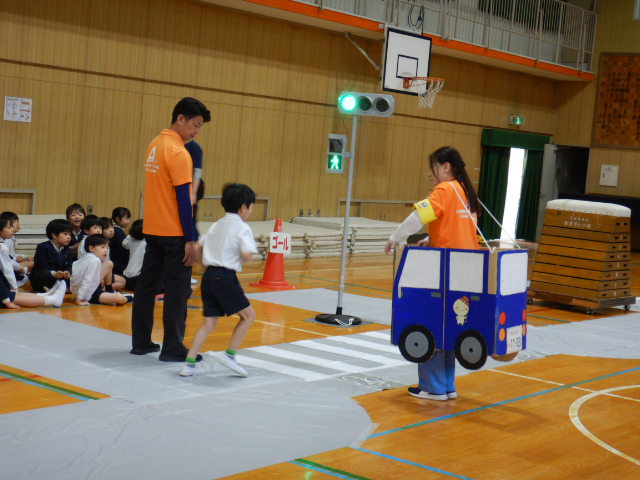 小学校の体育館で子どもに交通安全について教える区役所職員