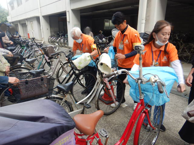 キャンペーン参加者の自転車前かごにひったくり防止カバーを取りつける区役所職員