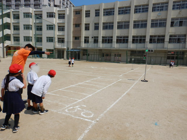 運動場に描いた横断歩道の安全なわたり方をアドバイスする区役所職員