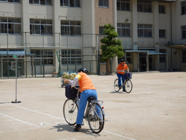 区役所職員が運動場に描いた道路を自転車で安全に走行する見本を見せる