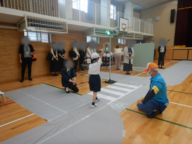 多くの保護者が見守る中、信号のある横断歩道を手を挙げてわたる児童
