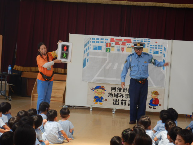 歩行者信号の模型を見せてルールを説明する警察官と区役所職員