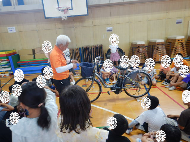 円になった児童の真ん中で自転車の点検の仕方を説明する区役所職員