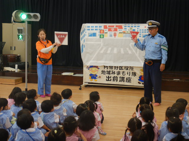園児に止まれの標識を見せて説明する警察官と区役所職員