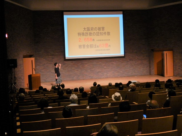 スクリーンに特殊詐欺の被害状況などを映写し説明する区役所職員