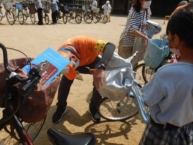 自転車前かごにひったくり防止カバーを取りつける区役所職員