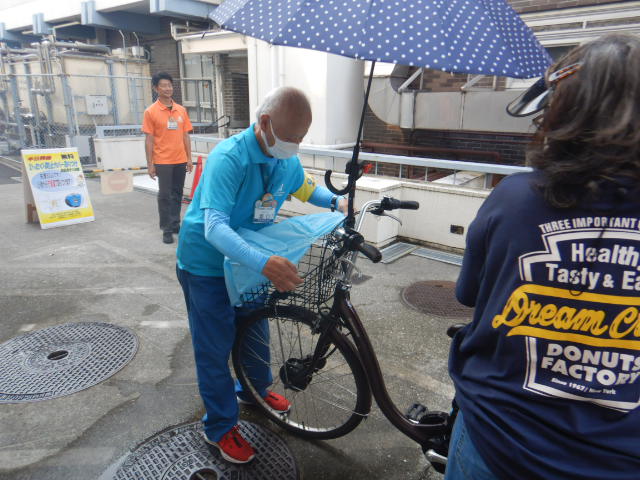 キャンペーン参加者の自転車前かごにひったくり防止カバーを取りつける区役所職員