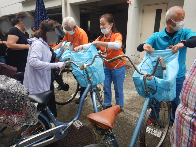 キャンペーン参加者の自転車前かごにひったくり防止カバーを取りつける区役所職員