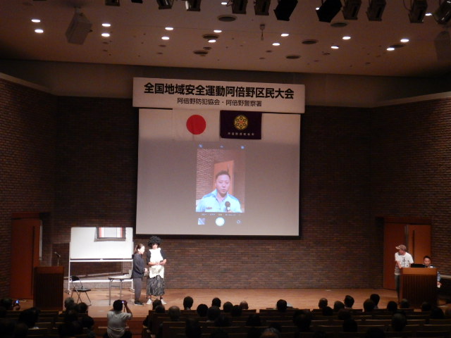 スクリーンに警察官を映し、テレビ電話を使った警察官を騙る詐欺を再現する