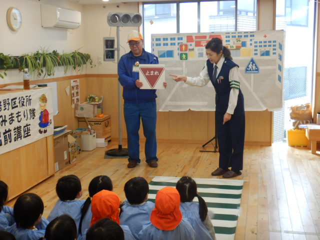 園児たちに止まれの標識を見せ、必ず止まって右左右を見ようと説明する警察官