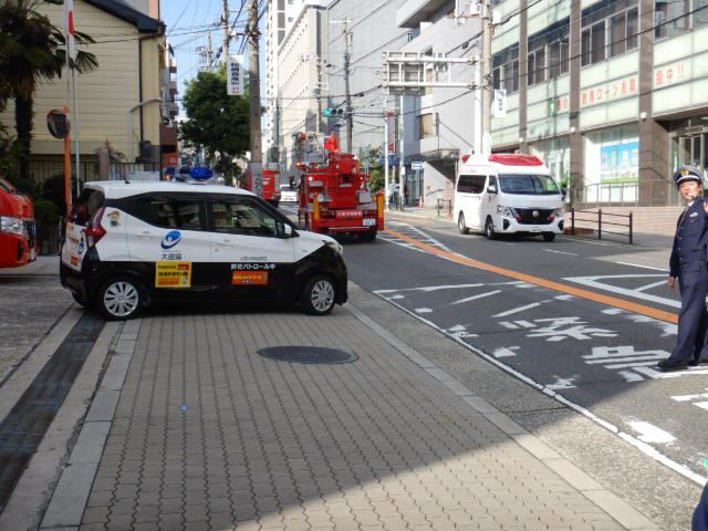 消防車両に続いて消防署を出発する青色防犯パトロールカー