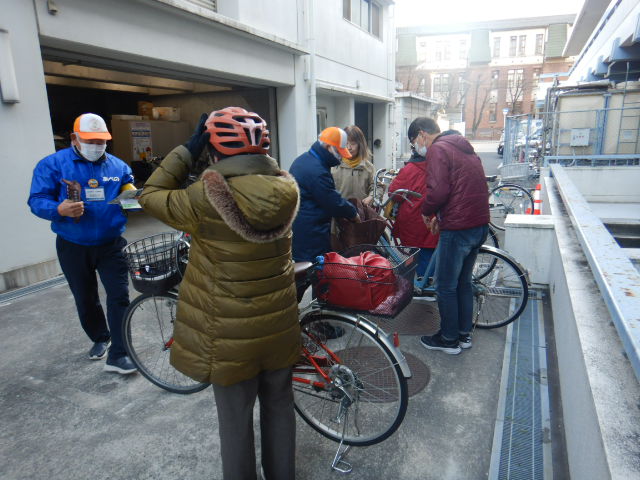 キャンペーン参加者の自転車前かごにひったくり防止カバーを取りつける区役所職員
