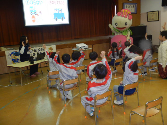 スクリーンに防犯クイズを映写し、正解の方に手を上げる園児たち