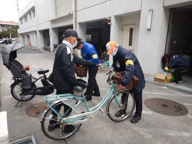 キャンペーン参加者の自転車前かごにひったくり防止カバーを取りつける区役所職員