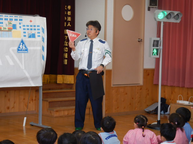 止まれの標識を園児に見せて説明する警察官