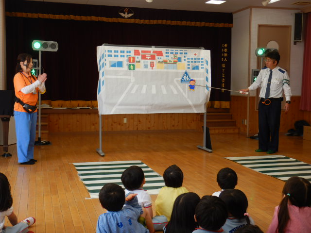 横断歩道の絵図を使って安全なわたり方を説明する警察官と区役所職員