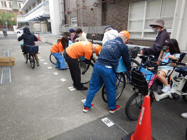 キャンペーン参加者の自転車前かごにひったくり防止カバーを取りつける区役所職員
