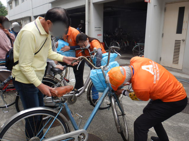 キャンペーン参加者の自転車前かごにひったくり防止カバーを取りつける区役所職員