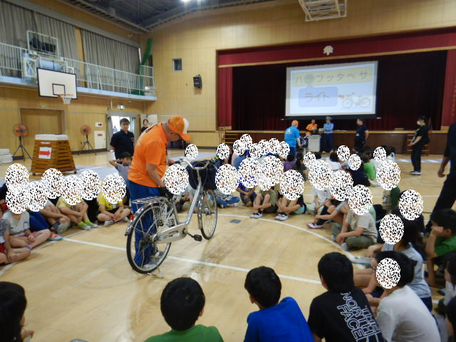 円になった3・4年生の真ん中で自転車の点検の仕方を説明する区役所職員
