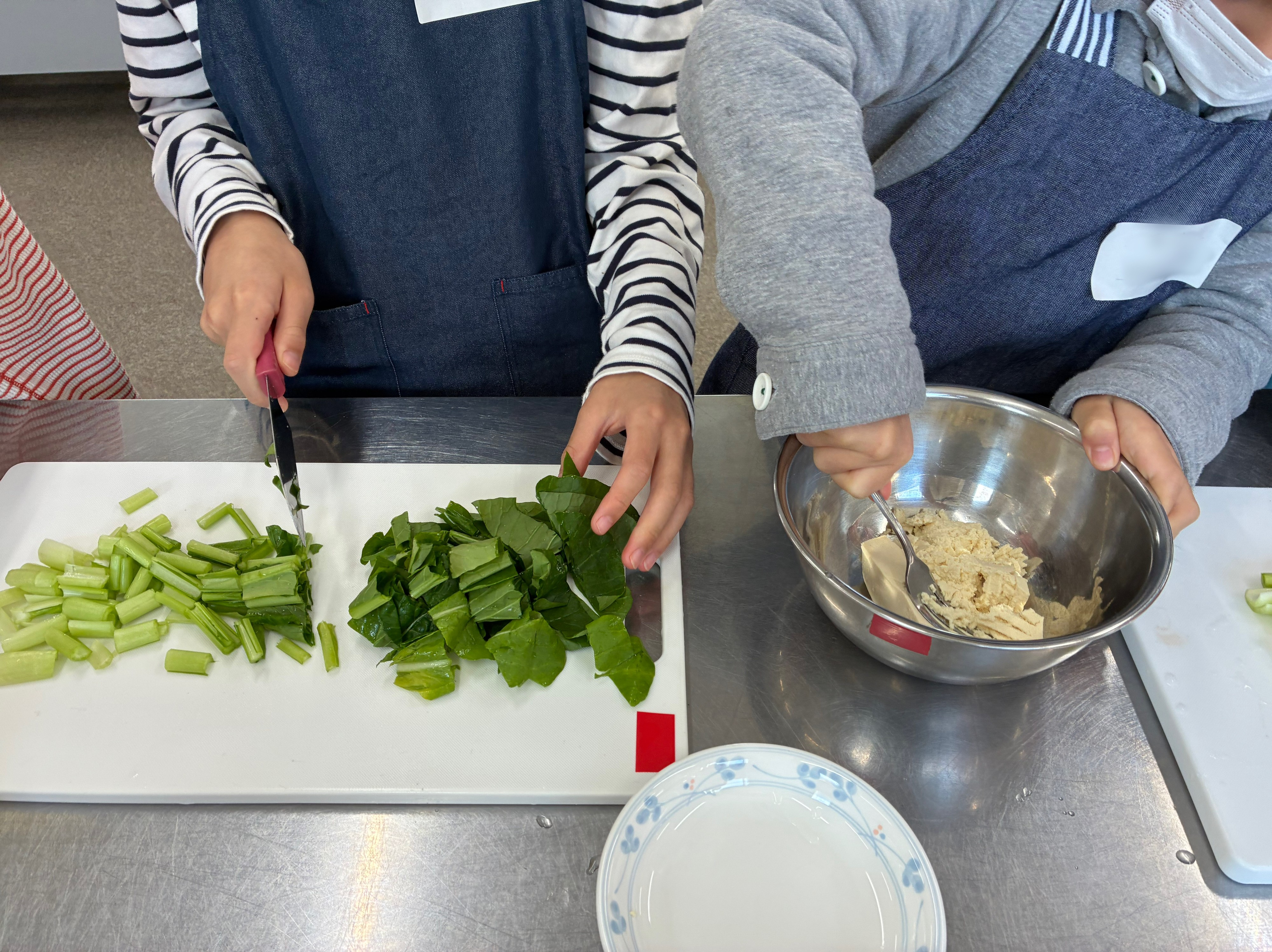 小松菜を切っている児童、豆腐をつぶしている児童の写真