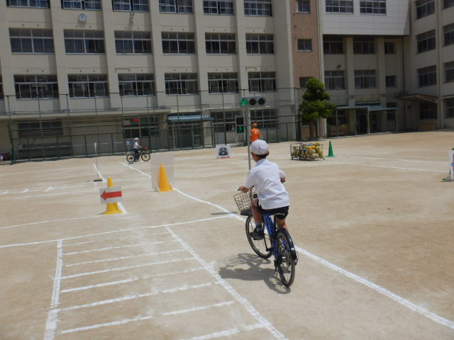 運動場に描いた道路上を自転車で安全に走行する児童