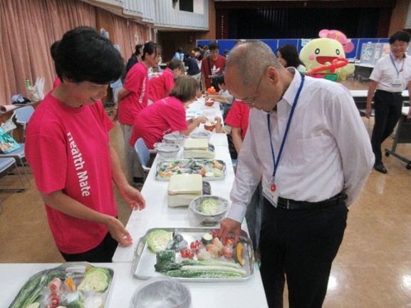 区長が野菜の重さ当てゲームをしている写真