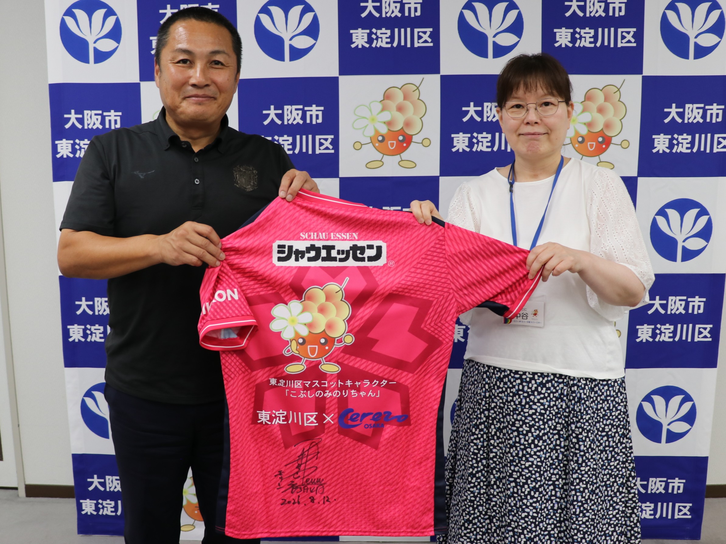 オリジナルデザインのユニフォームを掲げる森島会長と区長