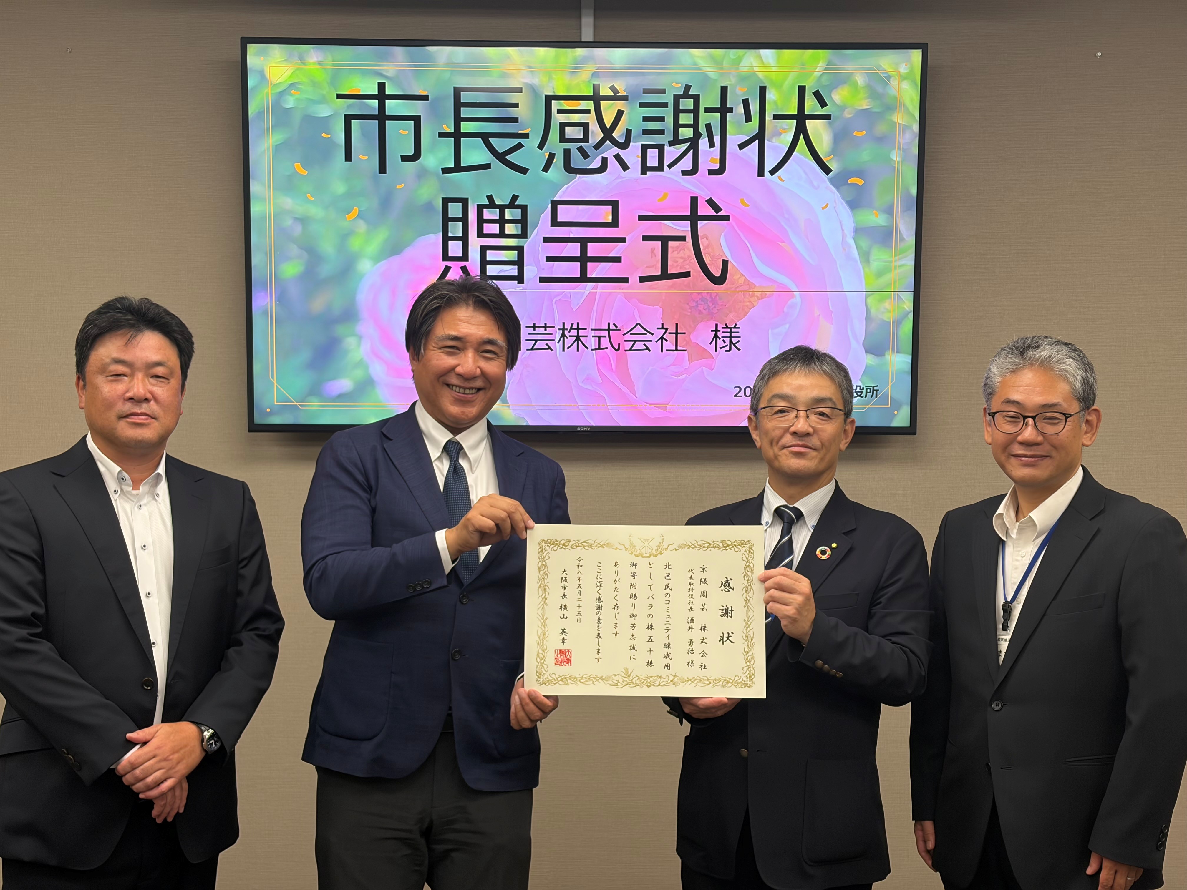 市長感謝状を持つ酒井社長と寺本区長、ほか2名の出席者