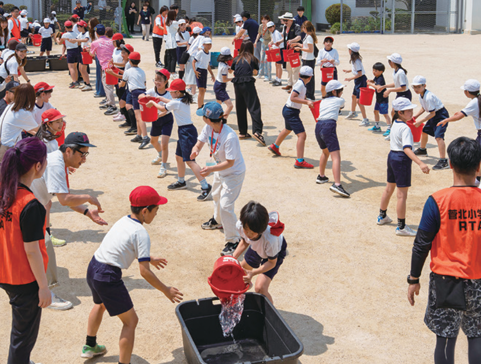 地域防災リーダーの指導のもとバケツリレーを行う菅北小学校の児童たち