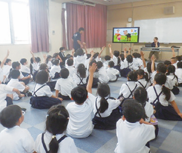 出前講座のクイズに元気よく手を挙げる小学生