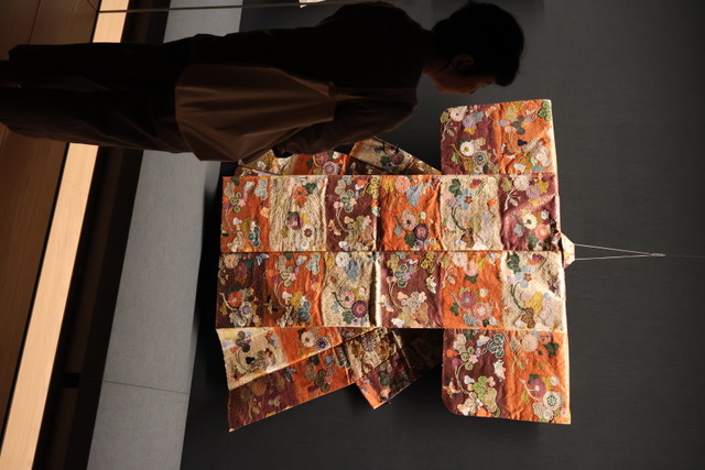 藤岡区長が紅白紫段三段〆切瓢箪菊文様唐織を観覧する様子
