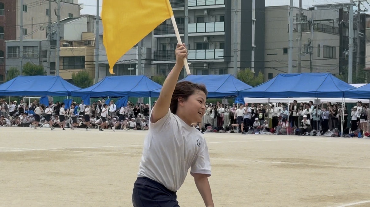 子どもが小学校の運動会で旗を掲げて走っている写真