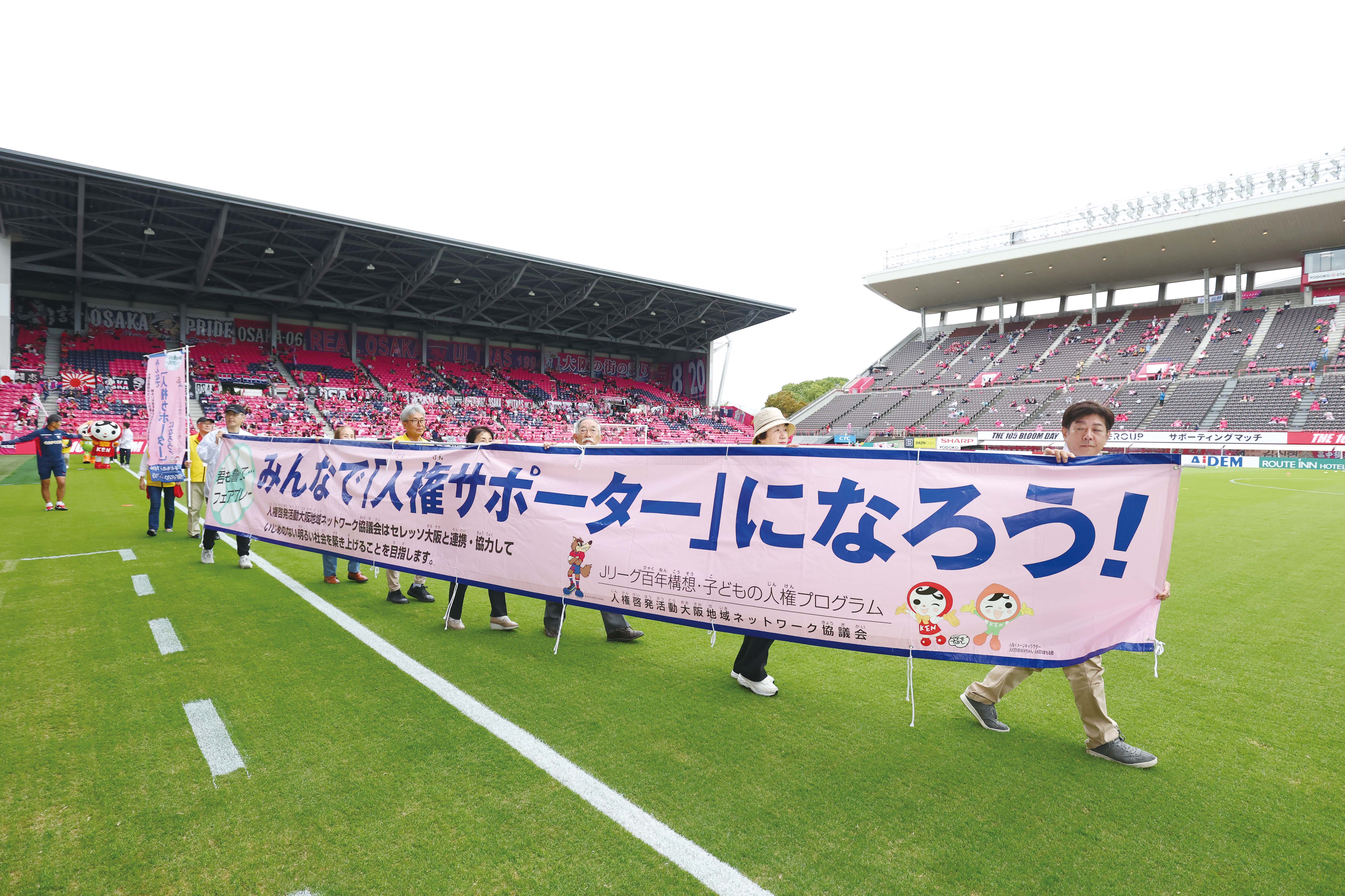 イベント参加者が人権啓発横断幕を掲げてピッチを周回している写真
