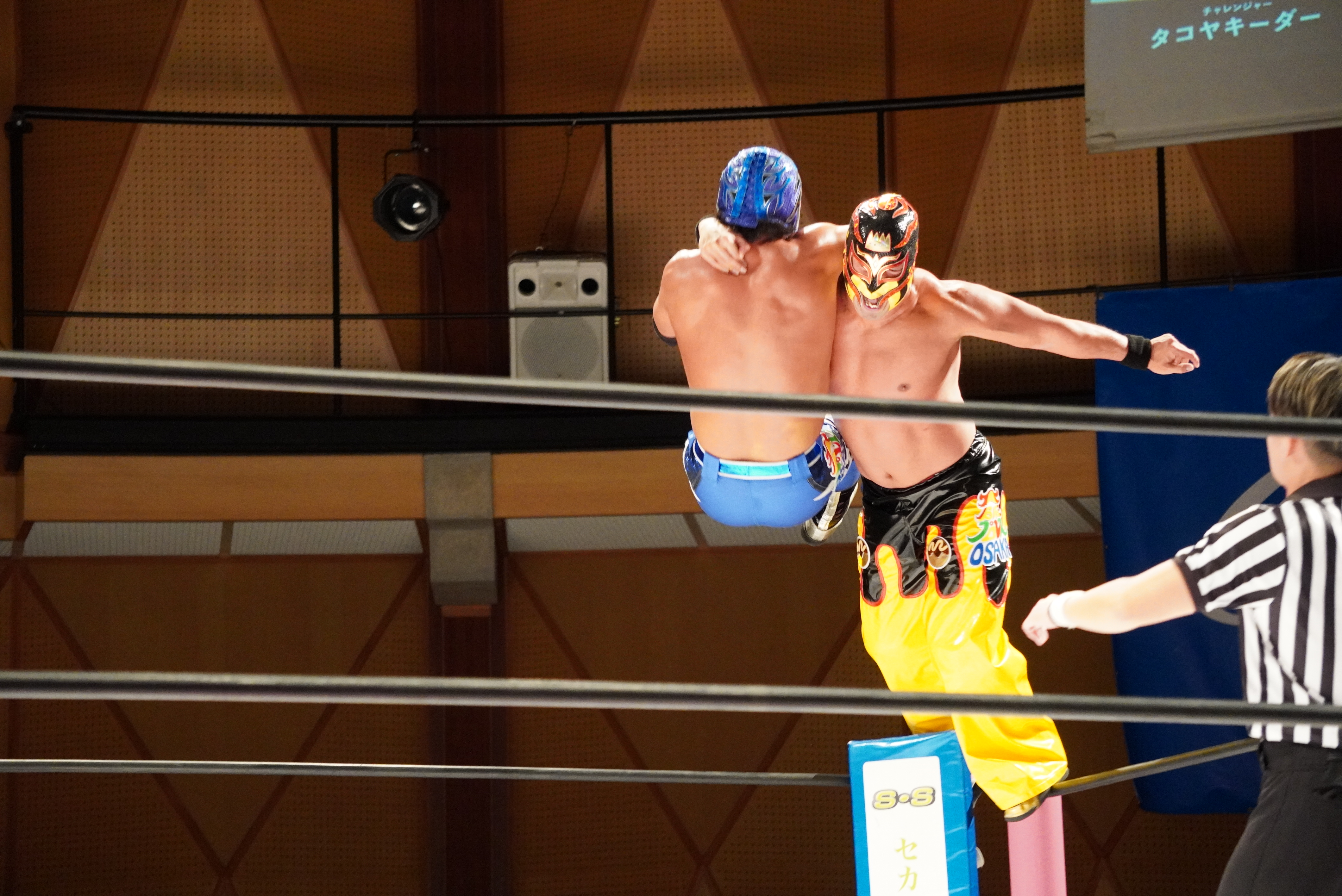 プロレスのリング上で、マスクを着けた選手2人が空中で激しく交錯している場面