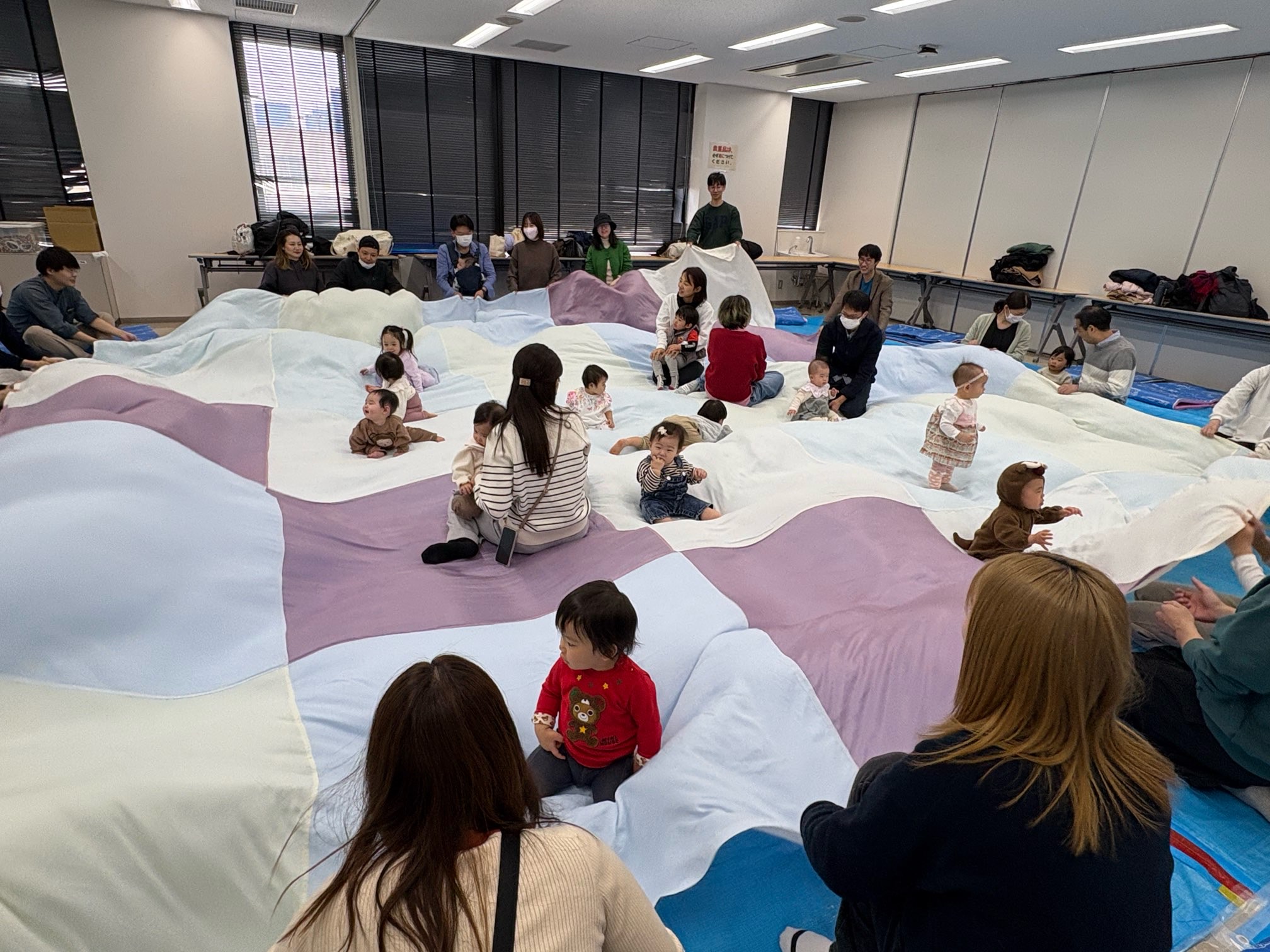 大きな布をみんなで円になって持ち音楽に合わせて揺らしている親子たち